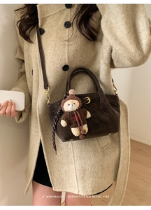 Detail of dark brown suede bucket bag with cute bear charm and gold hardware accents