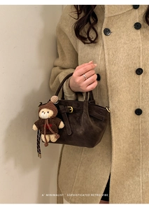 Detail of dark brown suede handbag featuring a decorative buckle and a cute bear charm
