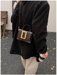 Detail of vintage dark brown leather crossbody bag with a large gold buckle on a model