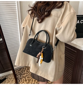 Détail d'un sac à main noir à damier avec pompon en perles de bois sur la bandoulière