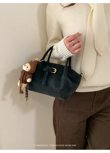 Close-up of black suede handbag featuring a buckle detail and a cute brown bear charm