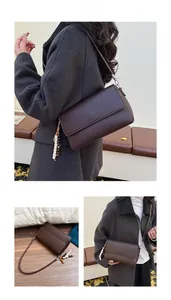 Detail der dunkelbraunen Leder-Umhängetasche mit Perlenanhänger und Retro-Klappendesign