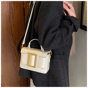Detail of cream white leather handbag featuring a large gold buckle on a model coat