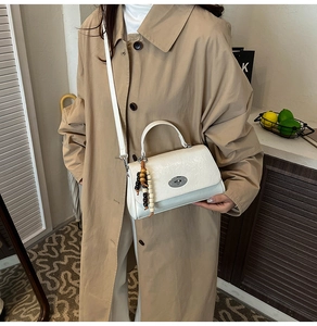 Detailansicht der weißen quadratischen Tasche mit Metallverschluss und Perlenanhänger