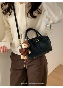 Detail of black suede bucket bag with gold hardware and a cute plush bear charm