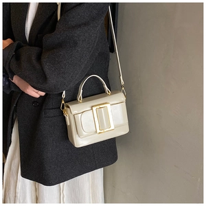 Detail of cream crossbody bag with large golden buckle and adjustable shoulder strap