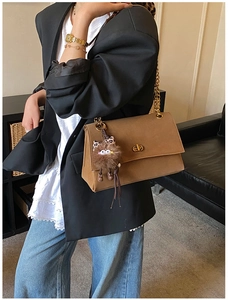 Detail of a brown leather messenger bag with gold twist lock and leopard bow charm