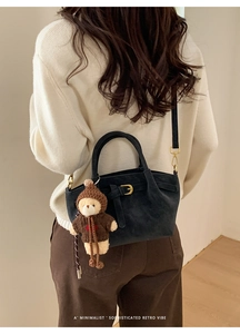 Minimalist black suede handbag with belt buckle detail and plush bear charm on model