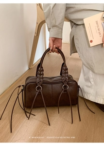 Detail of brown leather boston bag featuring metal eyelets and retro tassel charms