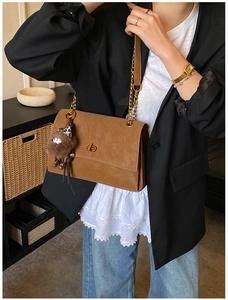 Detail of a matte brown messenger bag featuring a gold turn-lock and chain strap detail