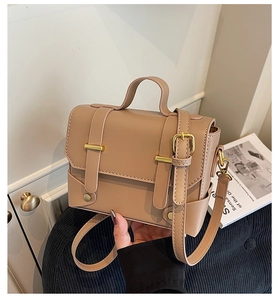 Detailed close-up of a khaki crossbody bag with dual straps and golden hardware buckles