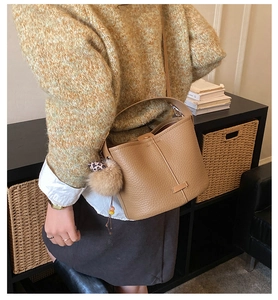 Close-up of brown pebbled leather bucket bag with leopard strap and pompom charm