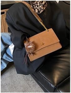 Detail of tan suede messenger bag with gold hardware and plush monster charm on model