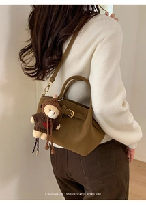 Brown suede handbag with gold buckle and a cute teddy bear charm on model's shoulder