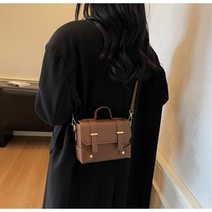 Detail of a brown vintage leather crossbody bag with gold buckles worn by a model