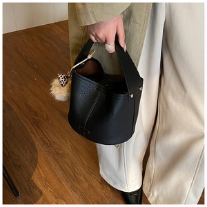 Detail of black lychee grain leather bucket bag with leopard print bow and pompom charm