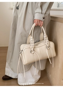 Detail of minimalist beige leather bag featuring woven handle and long decorative tassels