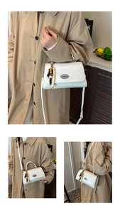 Detail der weißen Handtasche aus geprägtem Leder mit Drehverschluss und Perlenanhänger