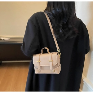 Detailed view of beige vintage crossbody bag with gold hardware worn by a model