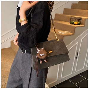 Detail of dark grey frosted leather bag with gold chain and plush owl charm on stairs