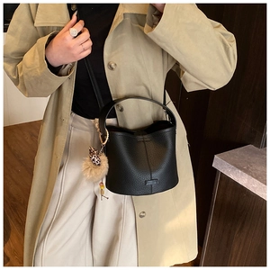 Detail of black pebbled leather bucket bag with leopard print fur ball charm on trench coat