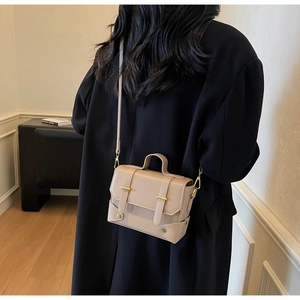 Detail of beige square crossbody bag with gold metallic buckles and top handle