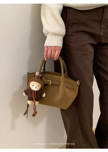 Detail of tan faux leather handbag with buckle strap and a cute teddy bear pendant