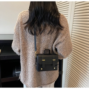 Detailed view of black leather crossbody bag with gold buckle hardware worn by a model