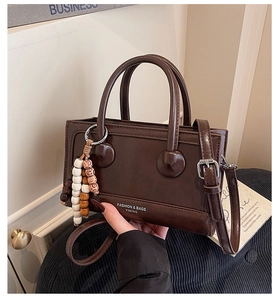 Detail of dark brown leather square handbag with top handles and wooden bead pendant