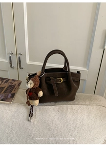 Detail of coffee brown suede tote bag featuring a gold buckle and a cute bear charm