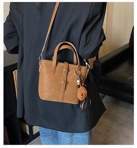 Sac cabas marron en similicuir avec breloque peluche porté par un mannequin stylé