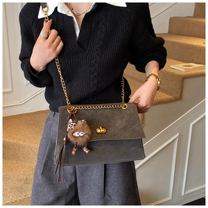 Detailed view of dark grey suede messenger bag with gold chain and plush charm