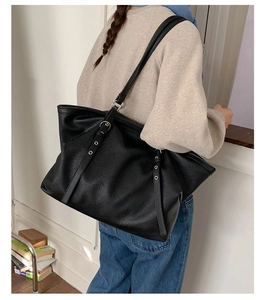 Detail of black pebbled leather tote bag with silver grommet straps shown on shoulder