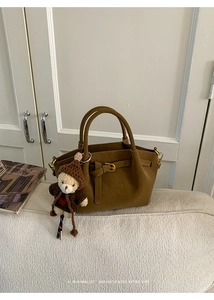 Detail view of brown suede bucket bag featuring decorative buckle and bear knit charm