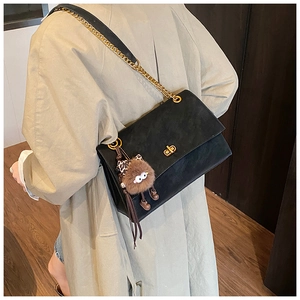 Detail of matte black messenger bag with gold chain and plush monster charm pendant