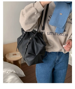 Detailed view of black lychee grain leather tote bag worn by model in cozy home setting
