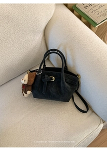 Detail of a black suede tote bag with decorative buckle and cute bear charm on a sofa