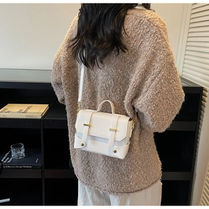 Rear view of a white vintage square crossbody bag with gold hardware worn over a sweater