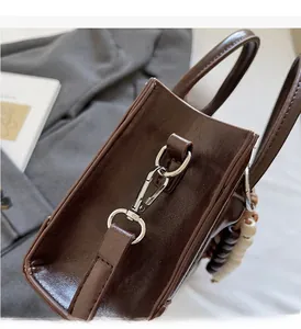 Detail of silver buckles and two-tone beaded charm on a dark brown glossy leather handbag