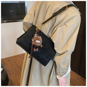 Detail view of black suede messenger bag with gold chain strap and plush monster charm
