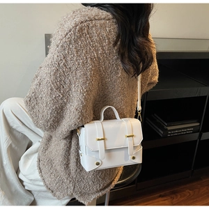 Detailed side view of white faux leather crossbody bag with dual gold metal buckles