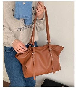 Close-up of brown pebbled leather tote bag with metal buckles and long shoulder straps