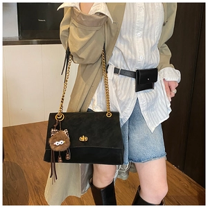 Detail of black matte flap bag with gold chain strap and cute plush monster charm accessory