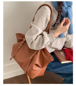 Detailed shot of brown litchi leather tote bag with metal eyelet strap on soft grey outfit