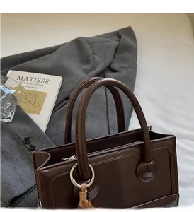 Detail of a dark brown leather baguette bag with sturdy round handles and metal hardware