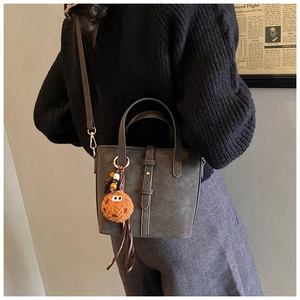 Detail der dunkelgrauen Leder-Eimertasche mit Tragegriffen und orangefarbenem Plüsch-Anhänger