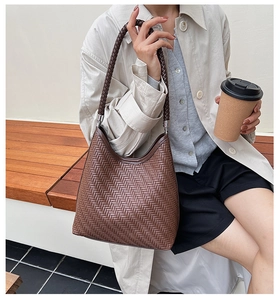 Close-up of brown woven bucket bag with metallic buckles and shoulder strap detail