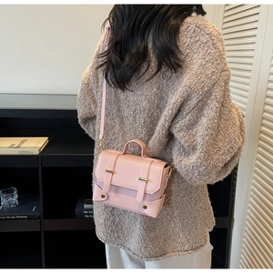 Detail of pink crossbody bag with gold buckles worn over a beige knit sweater