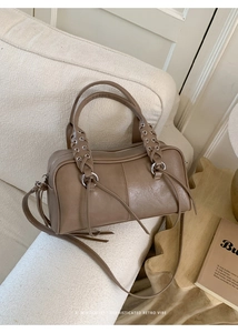 Detailed view of brown leather Boston bag with tassel charm on a textured sofa