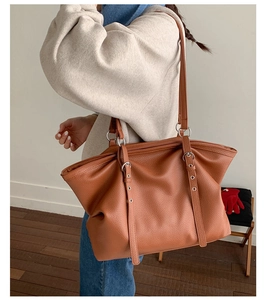 Close-up of brown pebbled leather tote bag with silver metal eyelets and adjustable strap